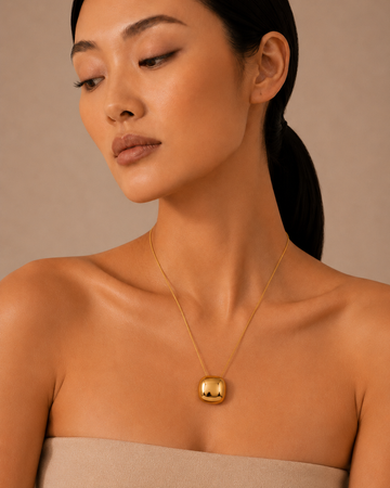 Gold necklace with a rounded pendant worn at the neckline