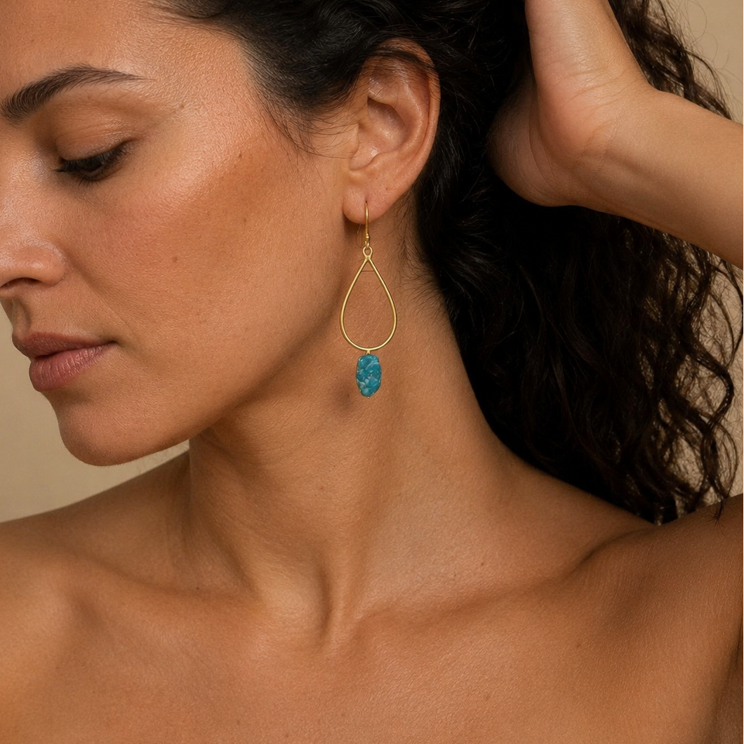 Blue Stillness Earrings worn on the ear, with open teardrop frames and blue stone drops