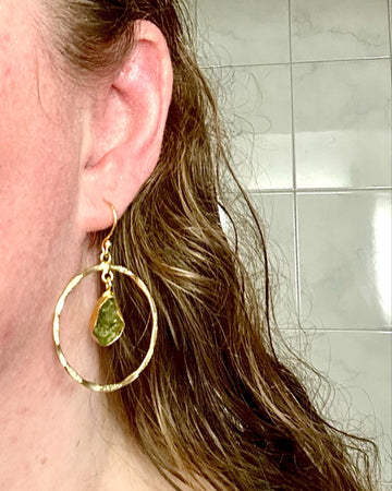 Gold-coloured hoop earring with a green stone drop worn on the ear