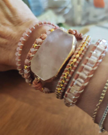 Pale layered bead bracelet with a pink stone centre worn on the wrist