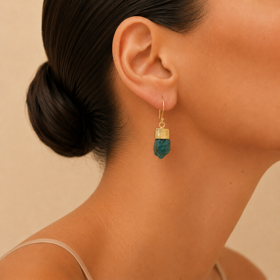 Ocean Spark Earrings worn on the ear, with rough blue stone drops with gold-coloured caps