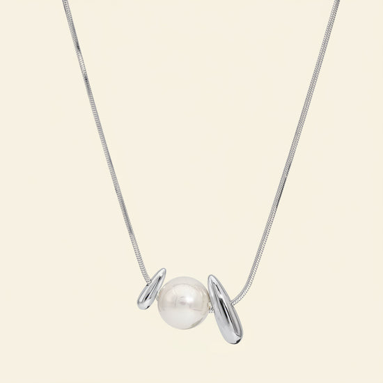 Pearl Embrace Necklace with a central pearl framed by curved metal details in silver finish