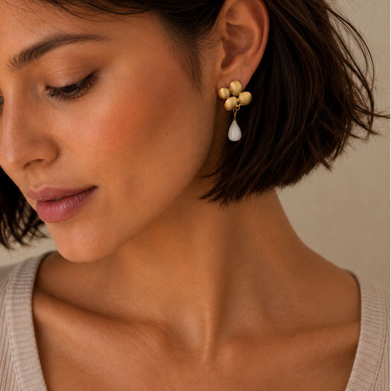 Petal Glow Earrings worn on the ear, with gold-coloured flower tops and pale teardrop drops