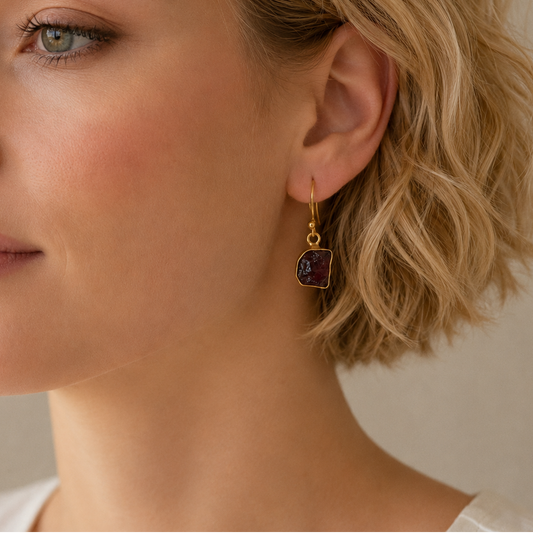 Quiet Flame Earrings worn on the ear, with dark purple stone drops with gold-coloured edges