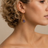 Quiet Halo Earrings worn on the ear, with purple stone drops inside open teardrop frames