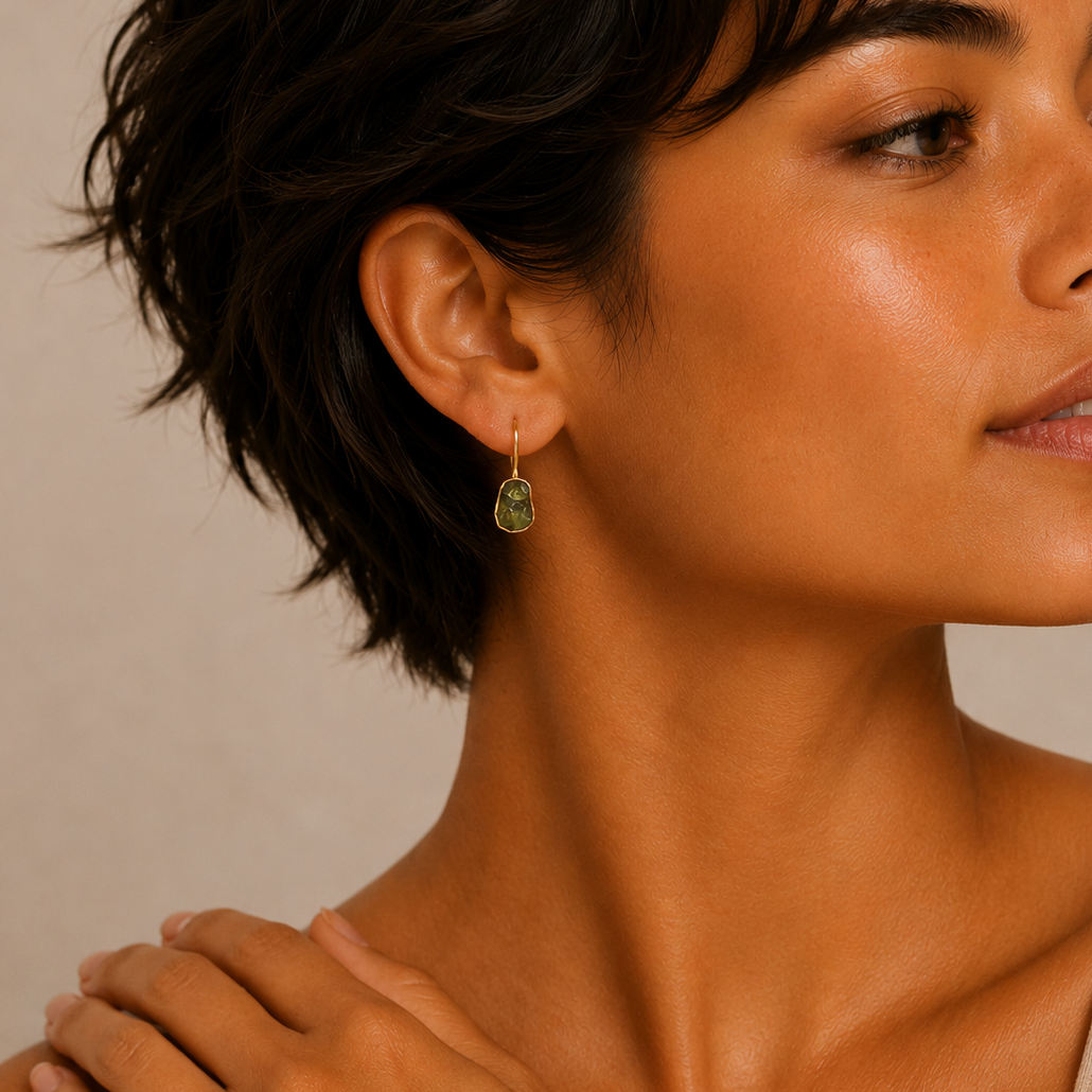 Quiet Leaf Earrings worn on the ear, with green stone drops on gold-coloured hooks