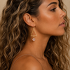 Soft Axis Earrings worn on the ear, with open triangular frames and pale pink stone drops