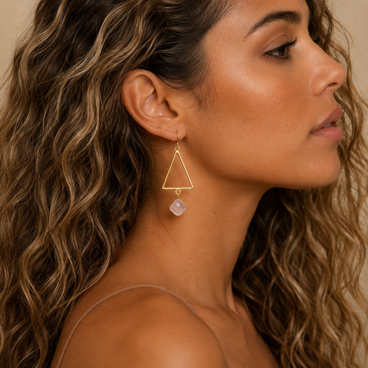 Soft Axis Earrings worn on the ear, with open triangular frames and pale pink stone drops